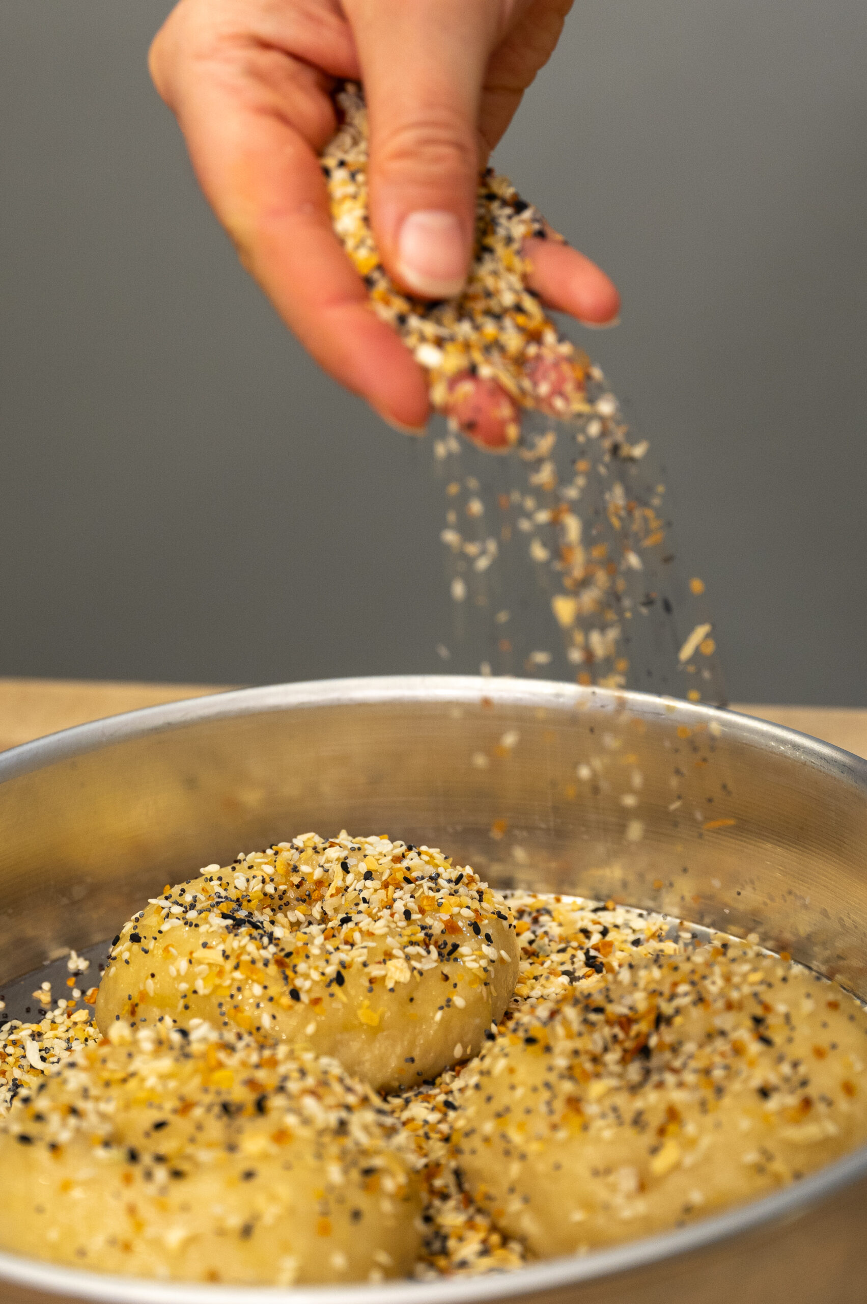 Everything spice being sprinkled over sourdough bagels