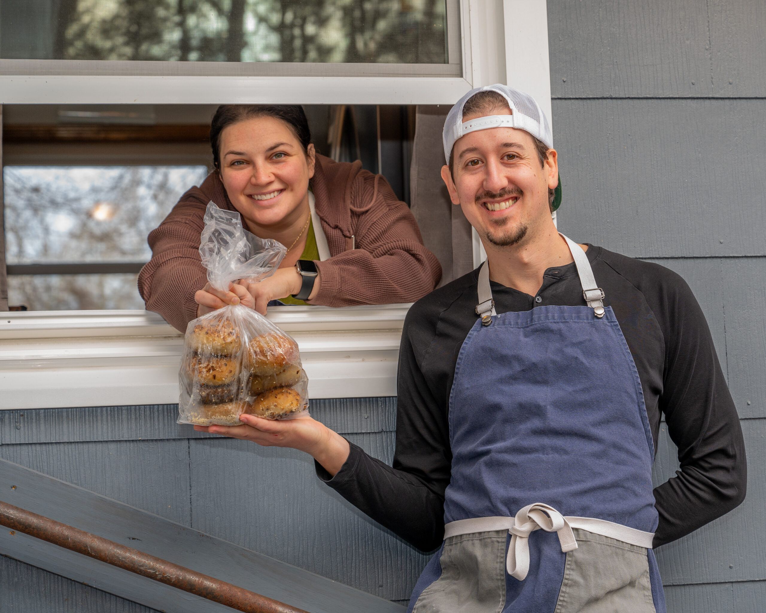 Steven and Lauren at the bagel window holding a bag of bagels